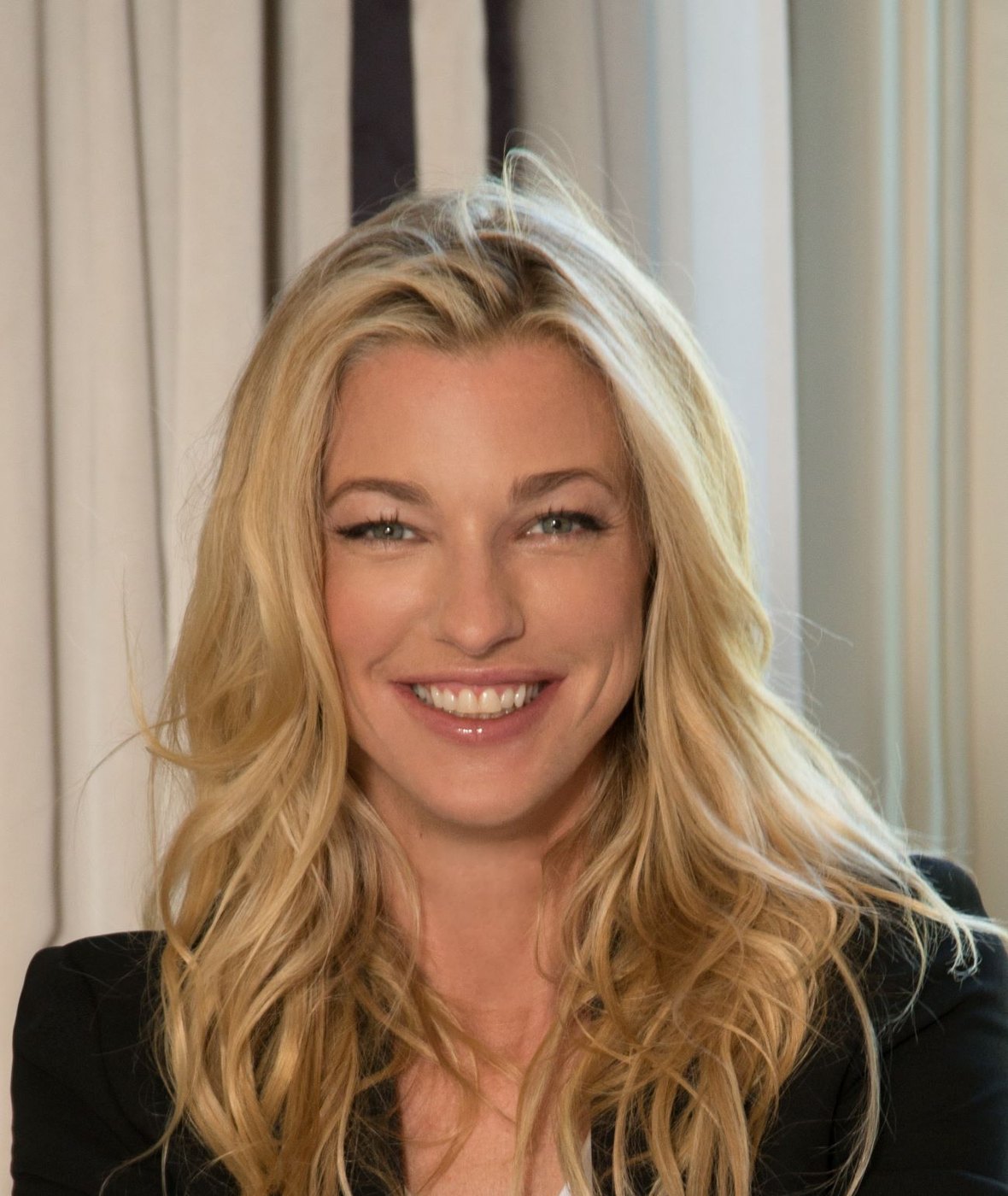Nicole Junkerman smiling warmly in a close-up portrait against soft curtains.