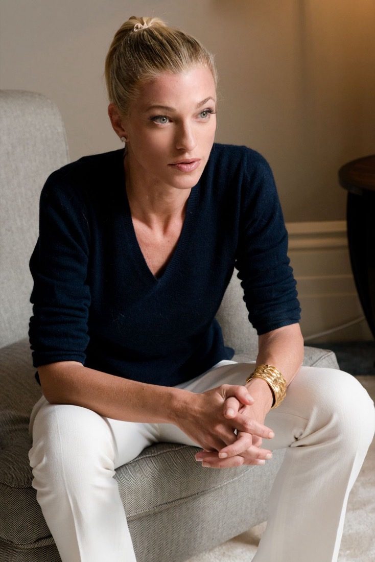 Nicole Junkerman seated calmly in an armchair with her hands clasped, wearing a navy top and white trousers.