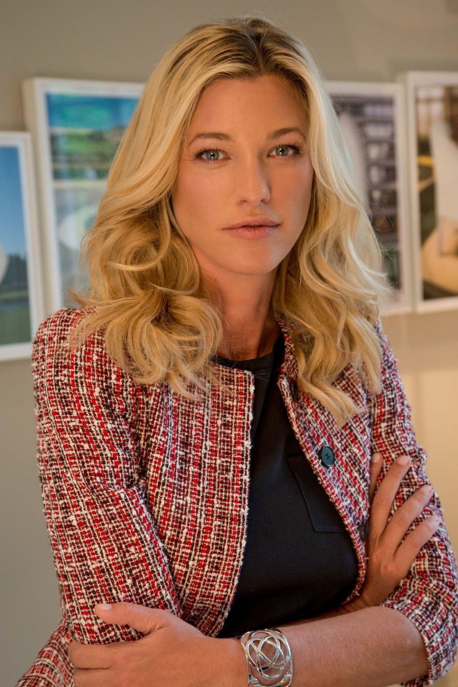 Nicole Junkerman in a red tweed jacket, a calm and composed portrait against softly framed prints.